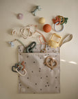 The mushie Water Resistant Wet Bag, beige with black floral prints, is open and spilling out pastel baby toys. Ideal for diaper bag storage, it keeps essentials organized and protected from moisture.