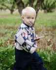 Toddler with FRIGG Daisy pacifier holds a notebook while walking in an orchard.