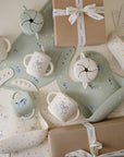 The mushie Bluey Gift Set features feeding essentials—handled cups, spill-proof snack containers, bibs, and pastel animal silicone placemats—arranged beside two white-ribboned gift boxes.
