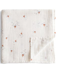 The mushie Organic Cotton Muslin Swaddle Blanket in the Boats color is shown neatly folded, with a corner turned up to reveal its soft reverse side.