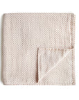 The mushie Organic Cotton Muslin Swaddle Blanket in Caramel Polka Dot is neatly folded and placed on a white background.