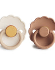 The FRIGG Daisy Natural Rubber Pacifier 2-Pack features two daisy-shaped pacifiers with scalloped edges, each with a natural rubber nipple and unique color accents. Both pacifiers are branded FRIGG.
