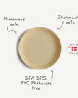 The Mushie Round Dinnerware Plate is beige, round, and made from non-toxic plastic that's BPA, BPS, PVC, and phthalate free. "Mushie" is embossed on it. Microwave and dishwasher safe. 100% made in Denmark with a Danish flag badge.