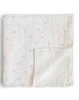 The mushie Organic Cotton Muslin Swaddle Blanket in Crowns is shown on a white background, with one corner turned up to reveal its small gold crown pattern.
