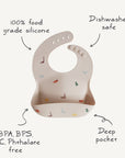 The mushie Silicone Baby Bib features colorful dinosaur prints, a deep pocket, and is made from 100% food-grade silicone. It's adjustable, non-toxic, BPA/BPS/PVC/phthalate free, and dishwasher safe for easy cleaning.
