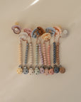 A row of mushie Silicone Pacifier Clip | Hera in pastel food-grade silicone beads, each in soft shades, is arranged neatly on a light surface for a minimalist look.