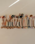 A row of mushie Silicone Pacifier Clip | Eva, with food-grade silicone beads in pastel and neutral tones, is arranged neatly on a glossy surface among other pacifier accessories.