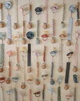 A neat wall display features FRIGG Rope Silicone Pacifier 2-Packs by FRIGG, showcasing colorful medical-grade silicone pacifiers with unique shapes, all arranged in rows as essential baby products.