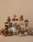 A neat pile of mushie baby toys, including the No-Drop Dino Teether (Tradewinds), features soft silicone in playful shapes like stars, animals, cupcakes, and clouds, arranged against a beige background.