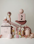 Pastel pink and beige baby toys surround the mushie Mini Toddler Bike.