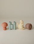 The mushie Nature Mold Free Bath Play Set features four adorable toy figures—a red mushroom, green binoculars, a cream-colored squirrel, and a brown acorn—perfect for nature-themed bath time on a neutral background.