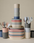 The mushie Square Dinnerware Plates, made from BPA-free plastic in soft pastel colors with a smooth matte finish, are stackable and displayed against a neutral beige background.