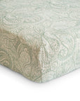 A close-up of the mushie Extra Soft Muslin Crib Sheet shows its green and white paisley pattern neatly fitted on a mattress—an ideal, breathable bedding choice for babies.