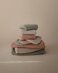 A neatly stacked pile of mushie’s Chunky Knit Pants in soft pastel hues like pale pink and sage green is shown against a plain beige background—perfect for any baby’s nursery.