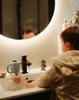 Lifestyle image of a child playing with bath toys in a sink, including the mushie Water Wheel Bath Toy and the Pirate Bath Play SEt.
