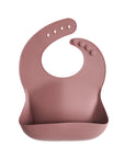 Mushie Silicone Baby Bib in pink with front pocket, adjustable buttons, and easy-to-clean design.