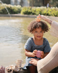 A woman crowns a smiling girl near mushie Mold Free Bath Play Set, easy to clean and safe.