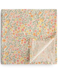 The mushie Organic Cotton Muslin Swaddle Blanket in Pastel Blooms, featuring a soft floral pattern, is shown folded with one corner turned up to reveal the reverse side.