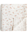 The mushie Organic Cotton Muslin Swaddle Blanket in Pink Flowers is shown folded with a corner flipped over, revealing the floral design on both sides. Made from soft, organic cotton with a plain white background.