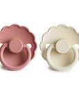 The FRIGG Daisy Natural Rubber Pacifier 2-Pack features two daisy-shaped pacifiers—one in dusty pink and one in cream—with natural rubber latex nipples, round handles, and "FRIGG" embossed on the bottom.