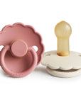 The FRIGG Daisy Natural Rubber Pacifier 2-Pack by FRIGG features two pacifiers with scalloped, daisy-shaped edges—one pink with a handle, the other white with a yellow latex nipple and no handle—displayed upright on a white background.