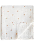The mushie Organic Cotton Muslin Swaddle Blanket in Sparrow, featuring light brown bird and star patterns, is neatly folded on a white background with one corner turned up to show the reverse side.
