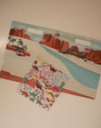Pair the mushie Reusable Sticker Set with a vibrant playset featuring a desert backdrop, red rocks, river, palm trees, and dinosaur toys—ideal for sparking creativity and imaginative play.
