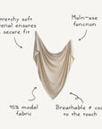 A beige, draped fabric with text: The mushie Stretchy Swaddle—95% modal—offers a breathable, cool-to-the-touch softness for a snug fit and versatile use as a baby blanket.