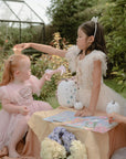 Three girls in princess dresses play outside, one crowning another as they sit at a table with pumpkins and flowers—reminiscent of the fun from the mushie Princess Mold Free Bath Play Set made from food grade silicone.
