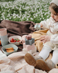 Toddler with stacking toys and a FRIGG Daisy Natural Rubber Pacifier at an outdoor picnic.