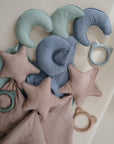 Moon Lovey Blankets by mushie, soft plush toys shaped like moons, are neatly arranged on a white surface in pastel blue, green, and taupe.