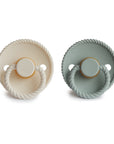 The Mushie FRIGG Rope Natural Rubber Pacifier 2-Pack includes two round pacifiers—one in light cream, one in soft muted green—with rope-textured edges, handles, ventilated shields, and natural rubber latex nipples. Essential for babies.