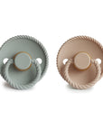 The Mushie FRIGG Rope Natural Rubber Pacifier 2-Pack includes sage green and beige pacifiers, each with a round textured edge, rope-like handle, and comfort-focused natural rubber latex nipple—perfect baby essentials.