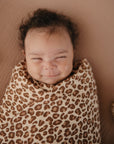Lifestyle image of a baby swaddled in organic cotton swaddle in Leopard