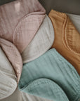 Two mushie Organic Cotton Muslin Burp Cloth 2-Packs in pastel pink, white, blue, and mustard yellow are beautifully arranged on a neutral background, highlighting their soft texture and gentle touch.