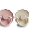 The FRIGG Daisy Silicone Pacifier 2-Pack by FRIGG features two medical grade silicone pacifiers—one in dusty pink and one in cream—with signature scalloped edges and round handles.
