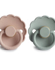 The FRIGG Daisy Natural Rubber Pacifier 2-Pack features two scalloped-edge pacifiers—one in muted pink, one in muted green—shown side by side on a white background. Each FRIGG pacifier has a natural rubber latex nipple.