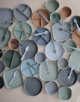 Mushie’s Square Dinnerware Plates are BPA-free plastic baby plates with divided sections, available in muted pastel colors like blue, green, tan, and gray.