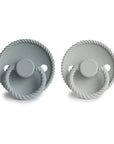 The FRIGG Rope Silicone Pacifier 2-Pack includes two medical-grade silicone pacifiers in light and pale grey, each with rope-like edges, circular handles, and the FRIGG name embossed on the front.