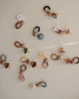 The mushie Silicone Pacifier Clip | Eva, made of food-grade silicone and featuring colorful beads in assorted shapes, is displayed on a light beige surface.