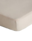 Close-up of a mushie Extra Soft Muslin Crib Sheet in beige, snugly fitted on a mattress corner, showcasing its smooth, breathable material and secure fit for your baby’s bedding.