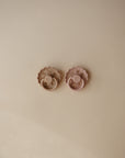 Two FRIGG Andersen Fairytale Silicone Pacifiers from FRIGG, featuring pastel colors and scalloped edges, rest side by side on a smooth beige surface with soft shadows.