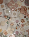A set of mushie Organic Cotton Muslin Burp Cloths (2-Pack) is arranged on a white surface among other baby essentials, with some items still in their packaging.