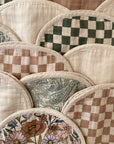 The mushie Organic Cotton Muslin Burp Cloth 2-Pack features rounded cloths with checkerboard, paisley, and floral patterns in beige, green, and brown scallop designs.