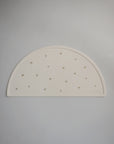 A semi-circular cream-colored silicone placemat by mushie, featuring small gold crowns and "mushie" embossed in the bottom right corner, displayed on a light gray background.