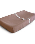 The mushie Extra Soft Muslin Changing Pad Cover in brown features two white safety straps and is shown on a white background.