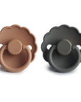 Two FRIGG Daisy Natural Rubber Pacifiers, one light brown and one dark gray, are side by side on a white background. Each features a scalloped edge, round handle, latex nipple, and "FRIGG" embossed at the bottom.
