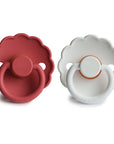 The FRIGG Daisy Natural Rubber Pacifier 2-Pack by FRIGG features two daisy-shaped pacifiers—one deep red, one white—with scalloped edges, circular handles, and natural rubber nipples, shown upright side by side on a white background.
