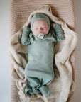 A newborn sleeps peacefully with a pacifier, dressed in soft green, on a striped cushion topped with the mushie Extra Soft Muslin Changing Pad Cover.