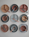 A top-down view of nine mushie Square Dinnerware Plates—BPA-free plastic plates for kids in muted pink, gray, and beige tones—arranged neatly in a grid on a white background.